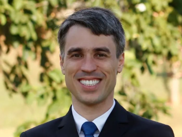 Retrato profissional de Pedro Rafael de Moura Meireles, advogado trabalhista, homem de meia-idade em traje social formal, terno escuro e gravata, sorriso confiante, fundo neutro cinza-claro, iluminação de estúdio suave, fotografia corporativa realista